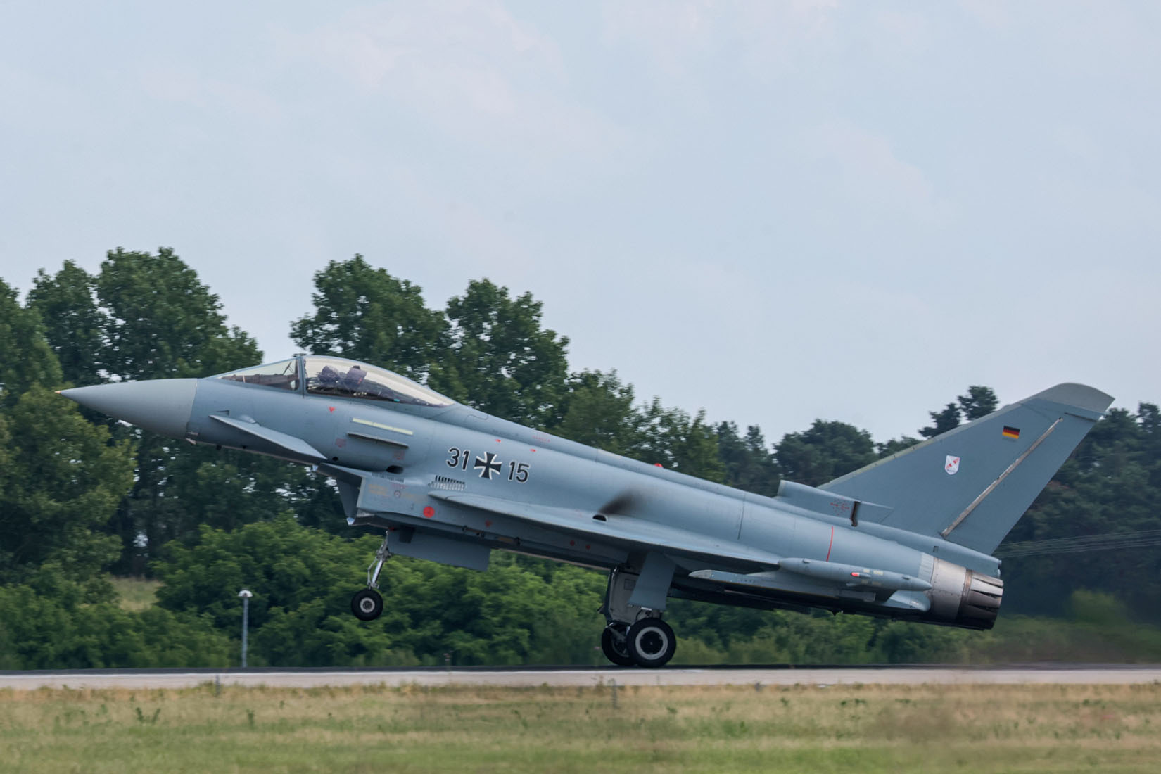 Ein Eurofighter-Typhoon hebt gerade ab, während er über eine grüne Landschaft mit Bäumen im Hintergrund fliegt.