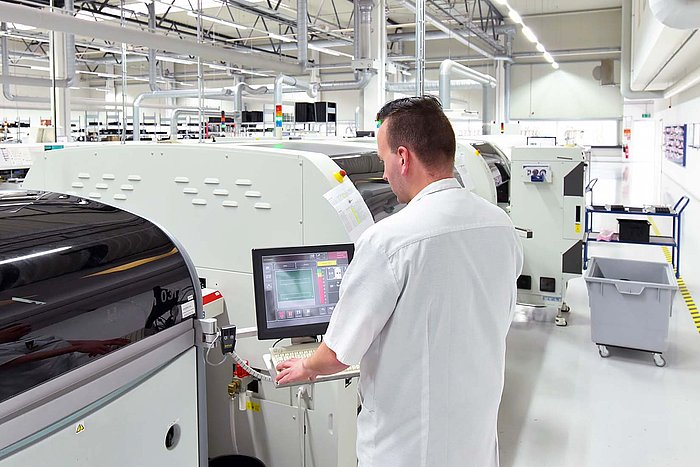 In einer hellen Fabrikhalle steuert ein Mitarbeiter eine Maschine, um den Produktionsprozess zu überwachen.