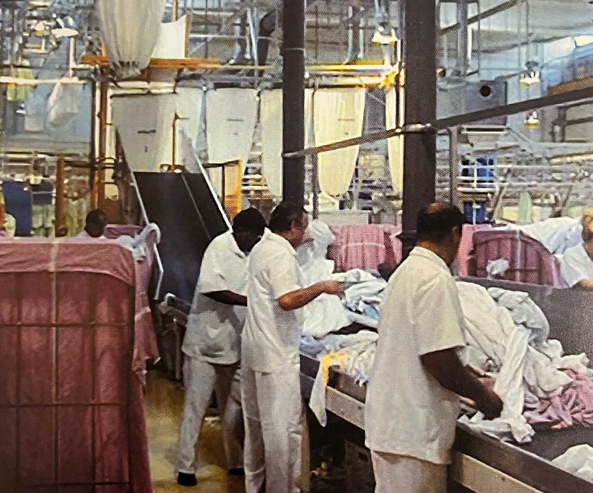Mitarbeiter einer Großwäscherei stehen am Fließband und sortieren Laken